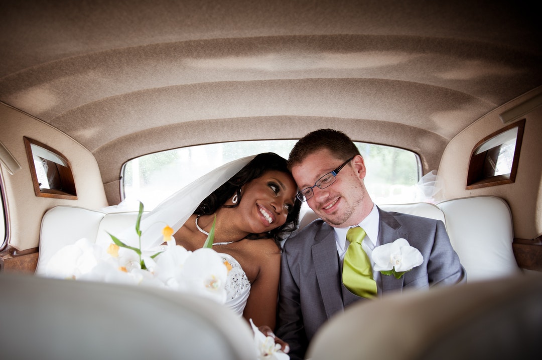 A bride and groom sitting in the backseat of a car and smiling in Amsterdam