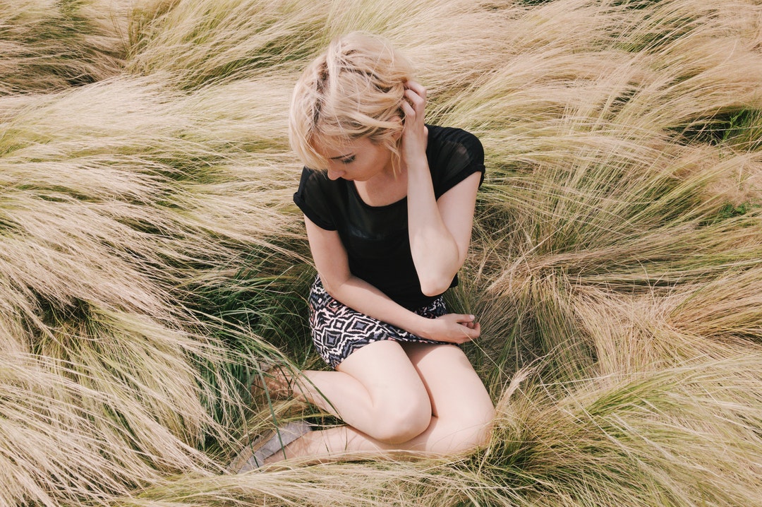 A blonde woman sitting in a field outside