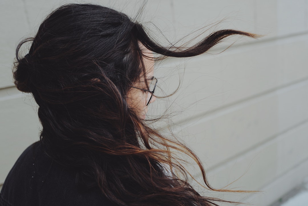 A brunette woman wearing glasses has hair blowing in the wind