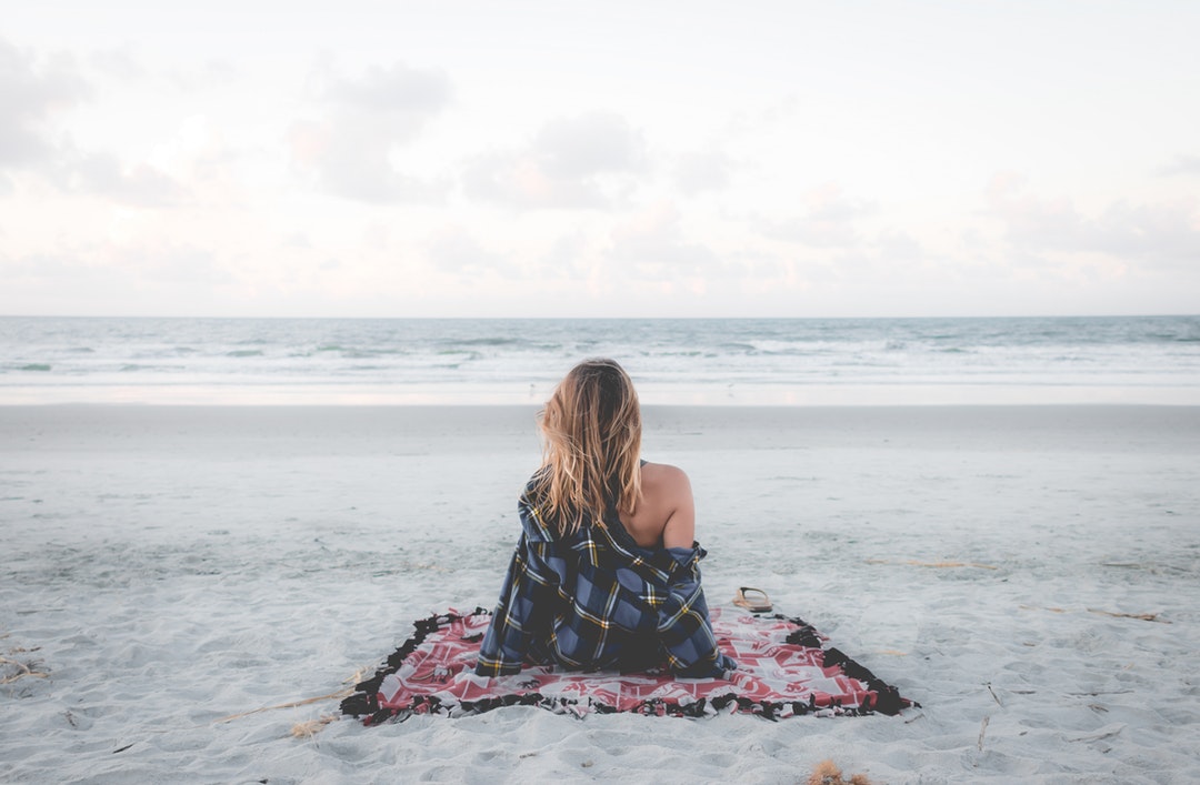 Young woman in checkered shirt sitting on a picnic blanket at the sand beach in Charleston