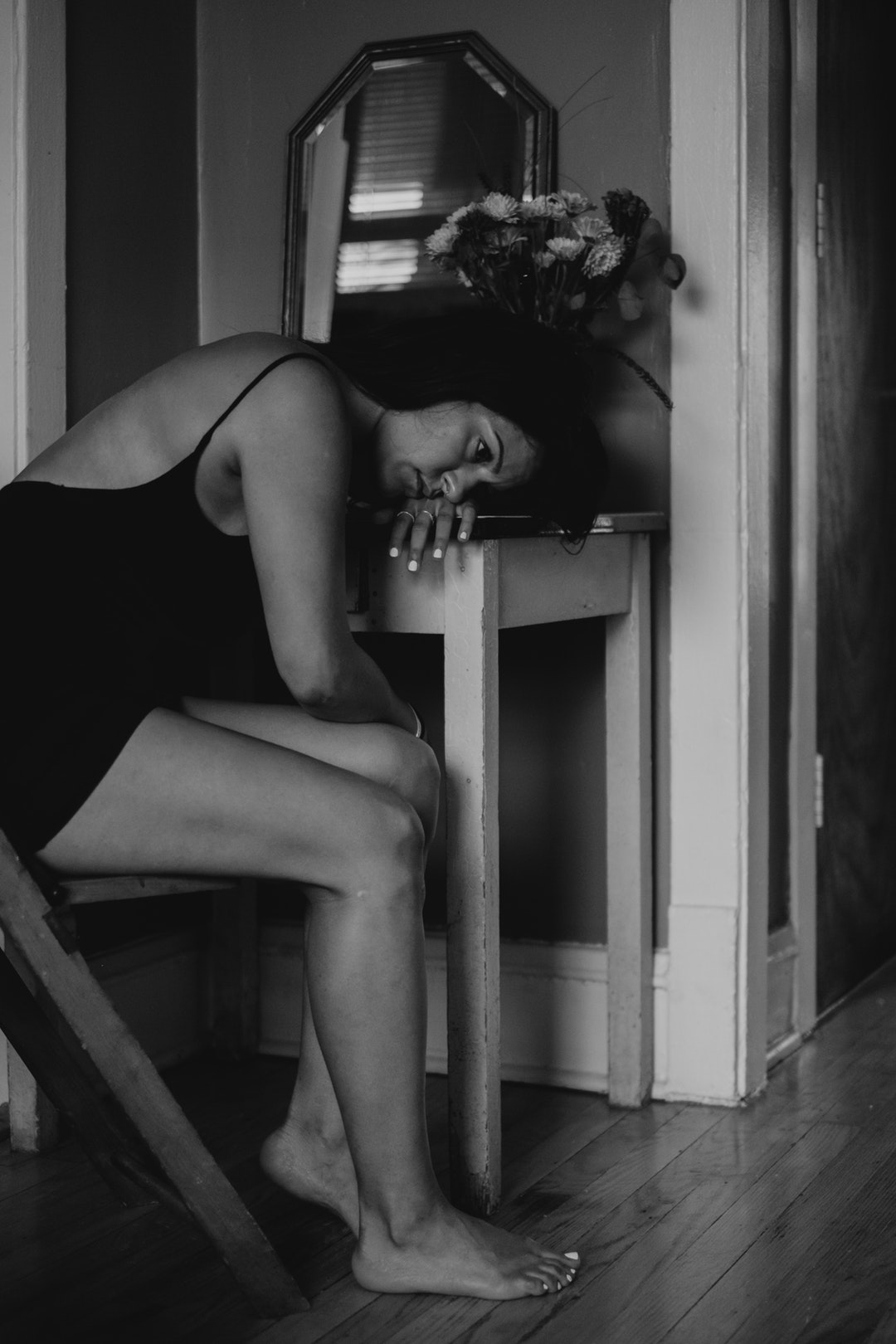 A sad woman in black and white with bare legs lays her head down on a table