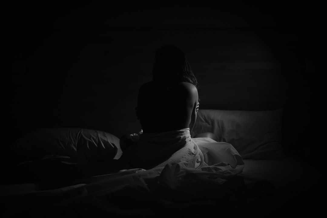 Silhouette of a shirtless person sitting alone wrapped in bed sheets