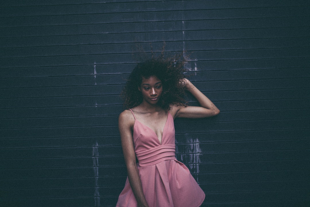 Woman in a pink cocktail dress looks unsure posed against a garage door