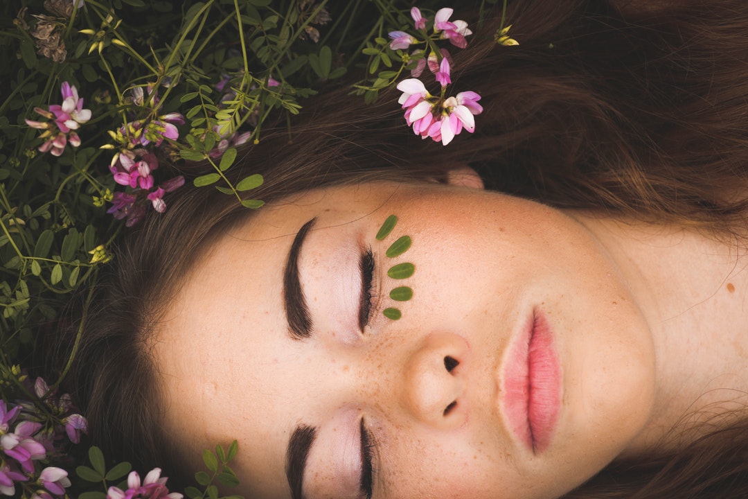 A woman lying on the ground with her eyes closed, wearing makeup under her eyes.
