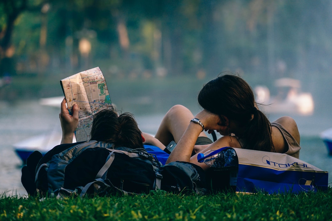Man and woman lying down in field on bags while looking at a map