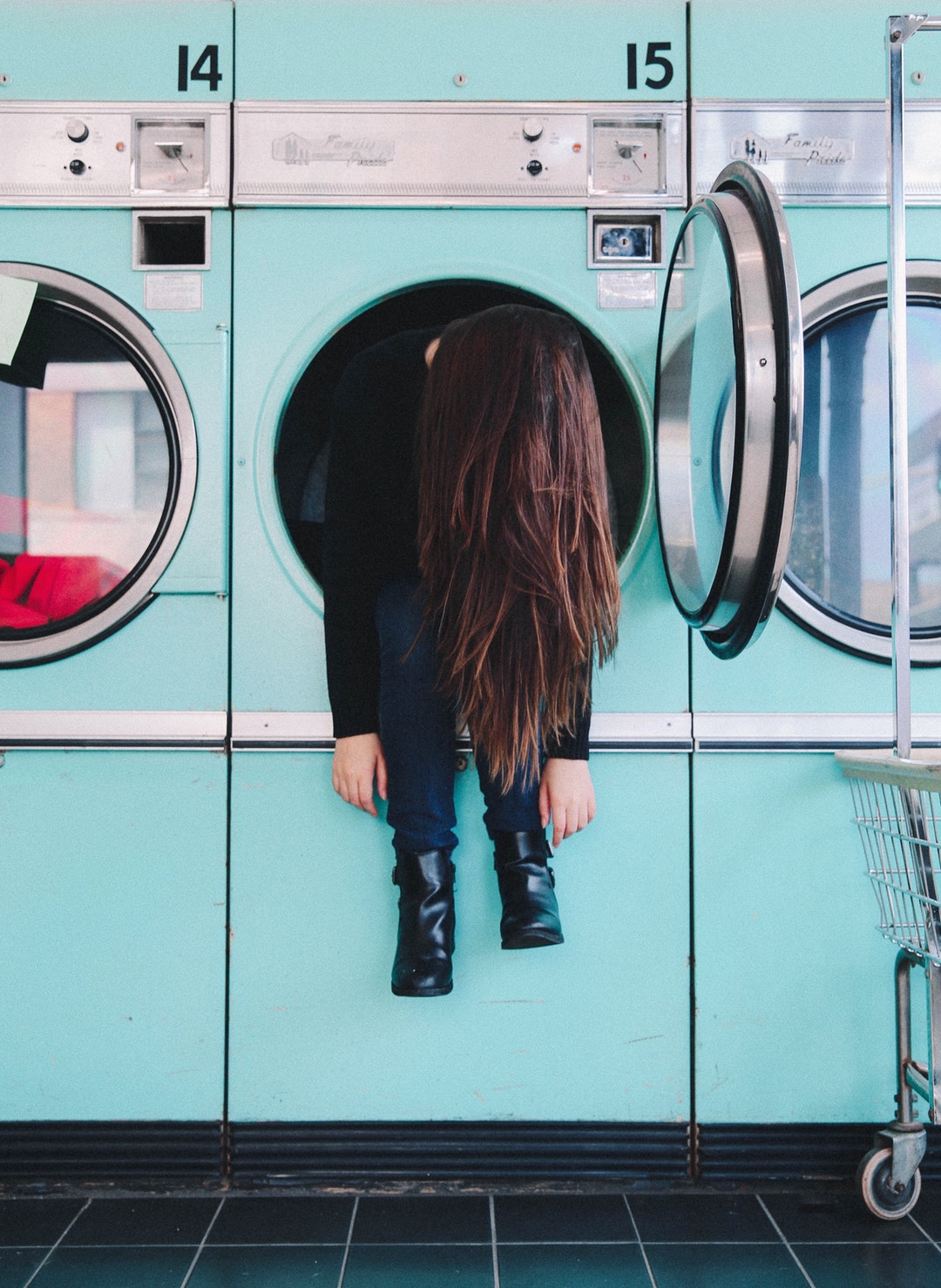 A person hanging out of a dryer at a laundromat.