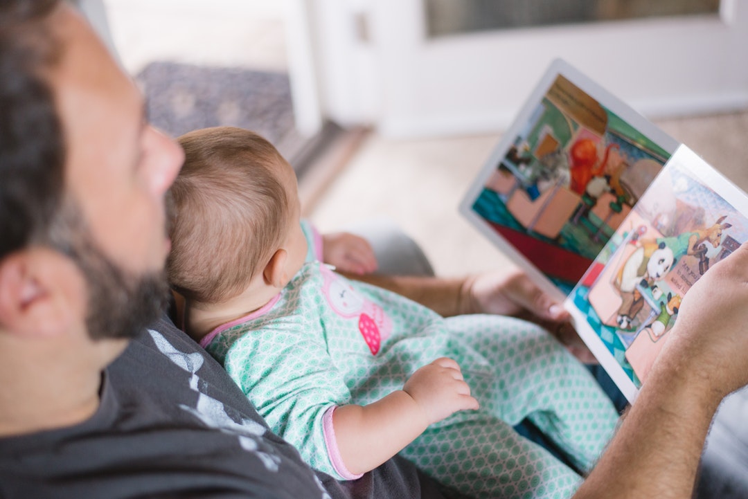 A baby sitting with her father while looking at a kids book.