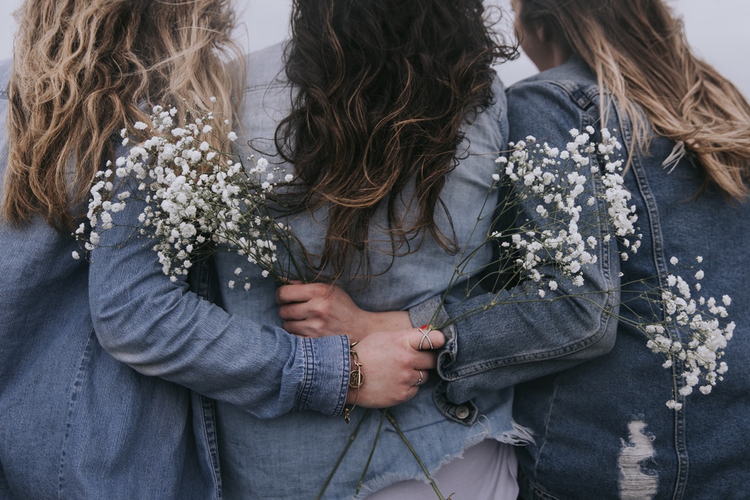 Three women holding each other, all wearing denim jackets.