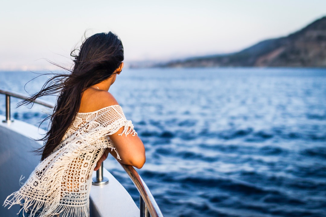 A woman staring out into the water while standing at the side of a boat.