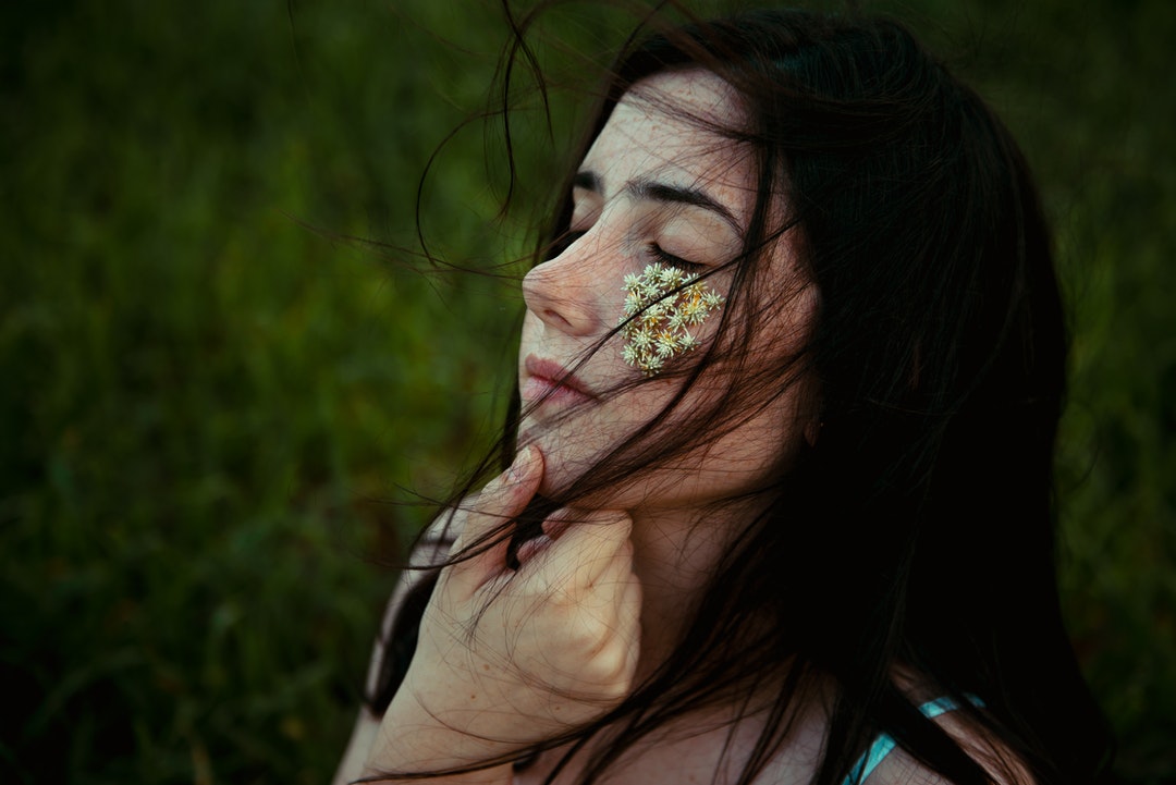 woman holding chin with white petaled flowers on right cheek