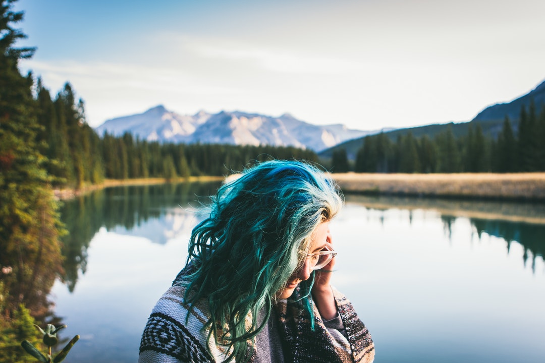 blue haired woman in grey top in front of body of water