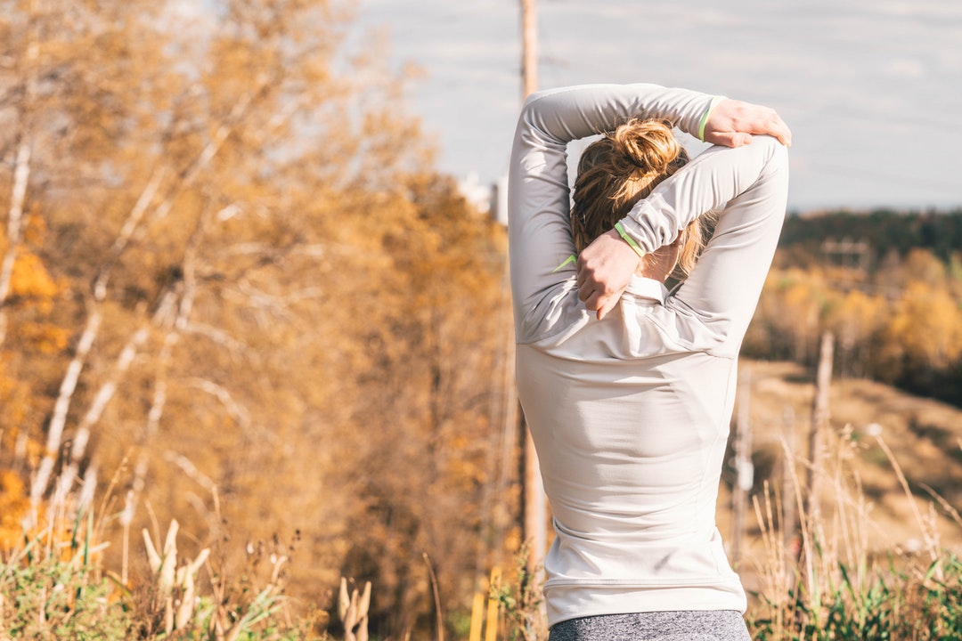 woman standing while stretching beside brown leafed trees