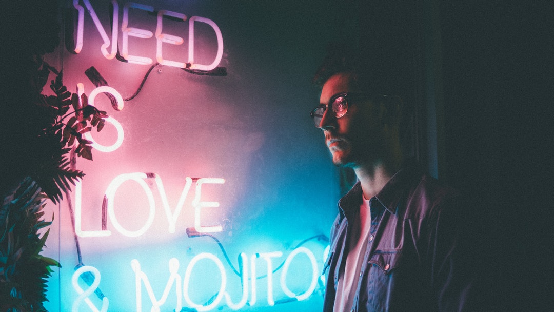 man standing beside white need is love and mojitos neon signage