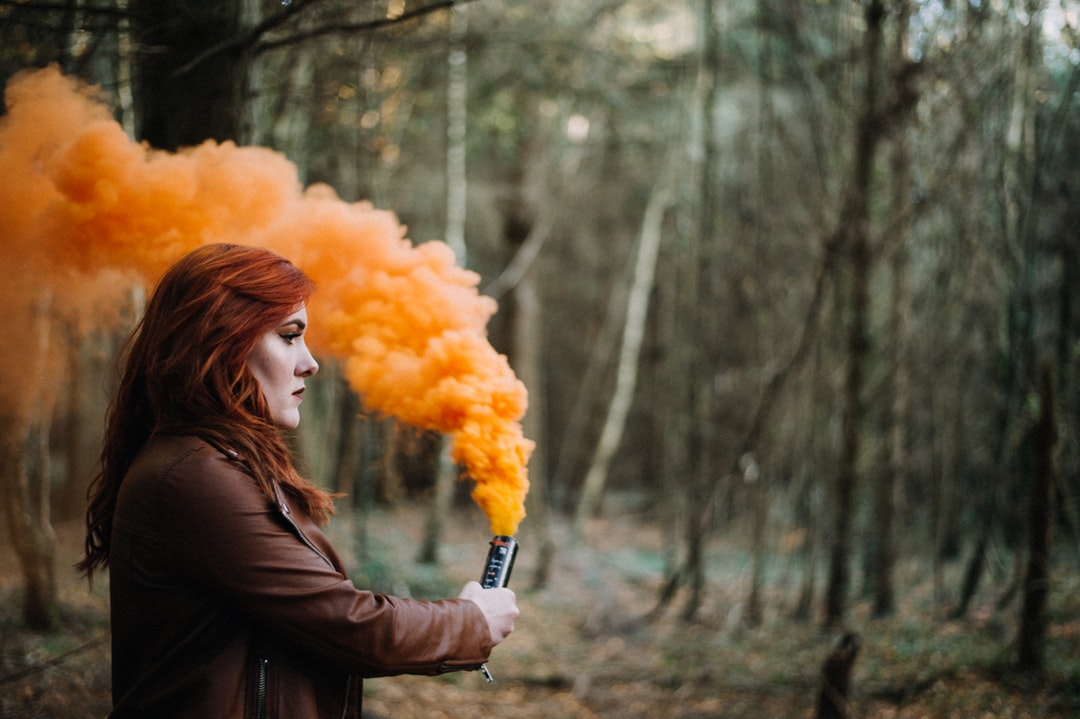 woman holding orange smoke powder surrounded with trees during daytime