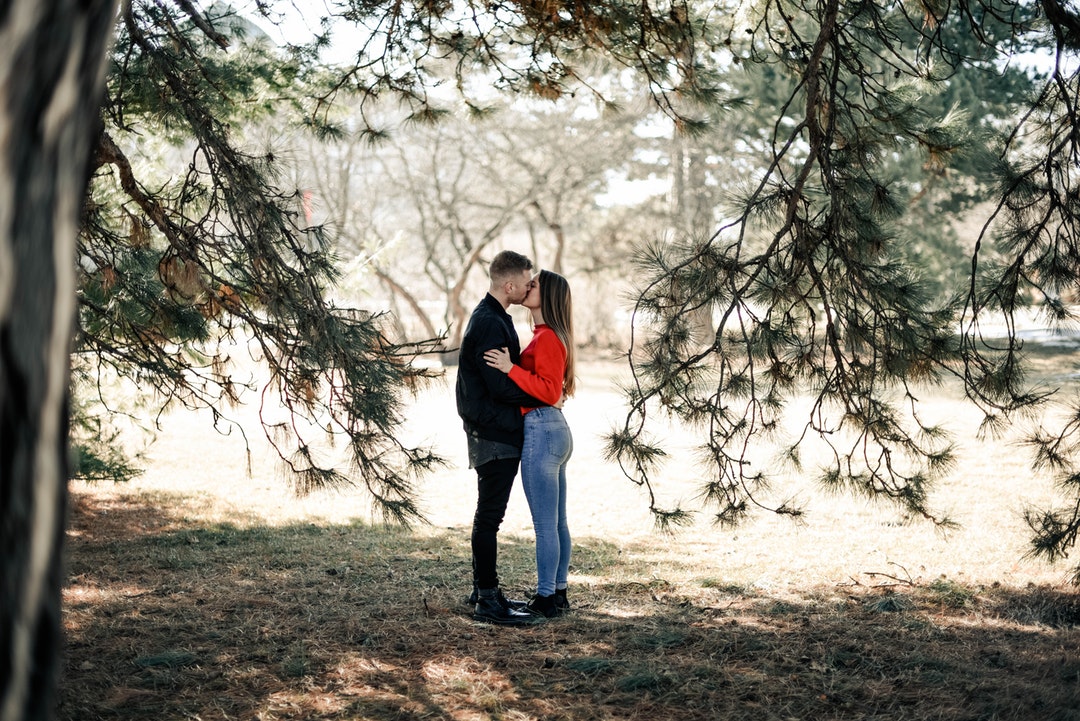 man and woman kissing underneath the tree