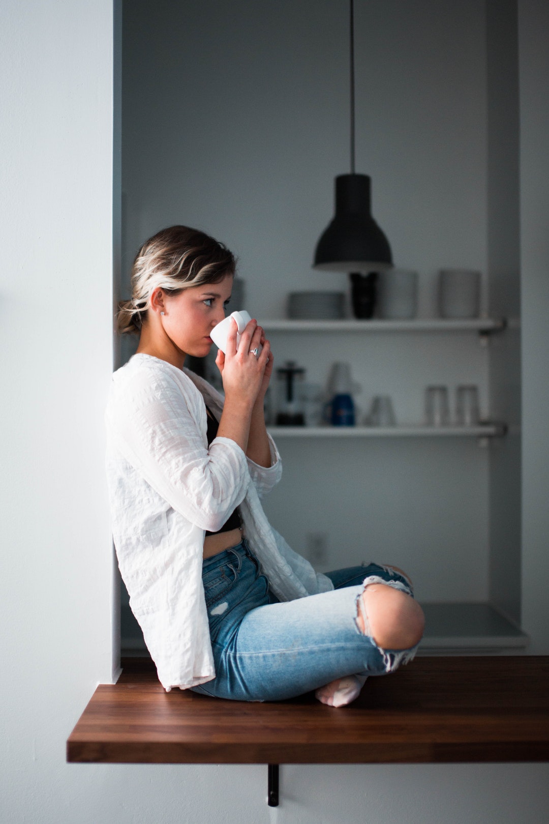 woman sipping cup white sitting on window