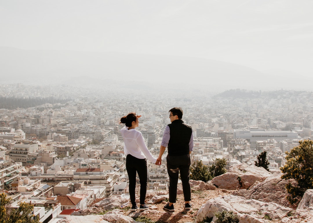 man and woman holding their hands together while standing on top of cliff