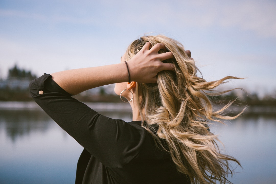 woman holding her blonde hair near body of water at daytime