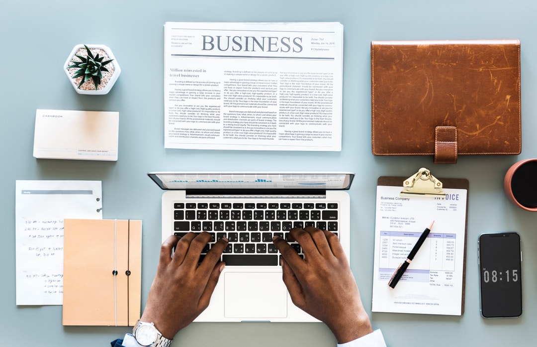 person using gray laptop with newspaper, flowers, and pens