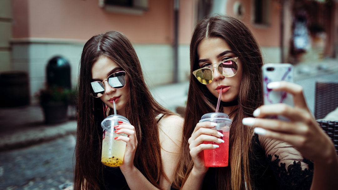 two women taking selfie while sipping straws