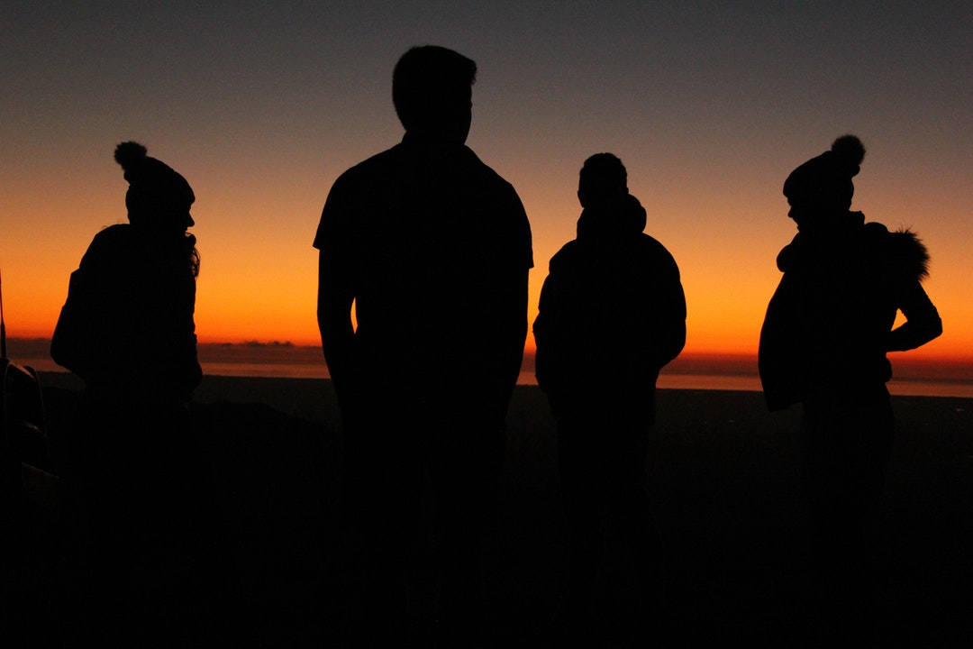four persons standing during sunset