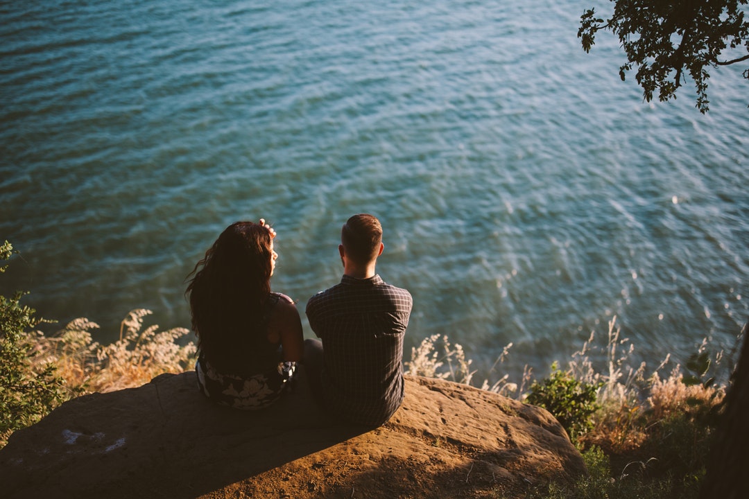 couple sitting on rock near body of water
