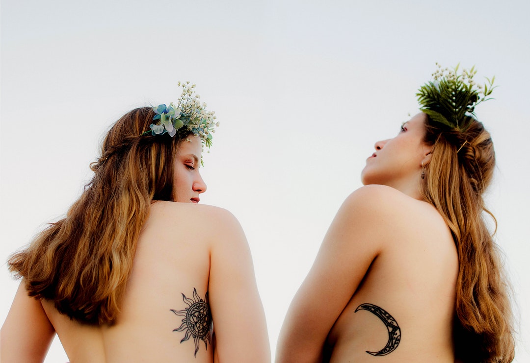 two naked women with sun and crescent moon tattoos