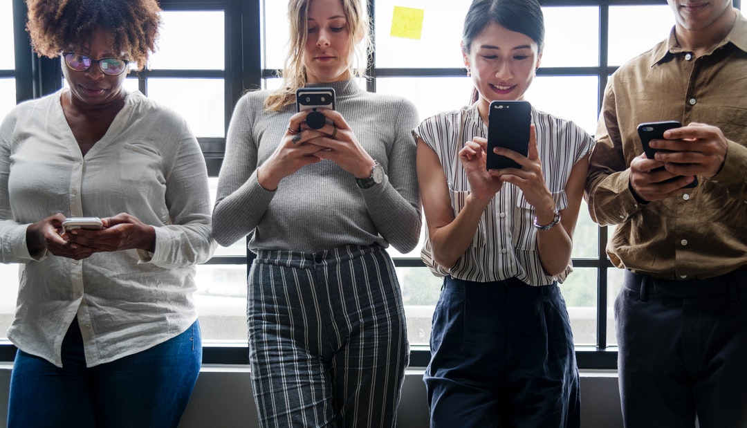 four person holding phones