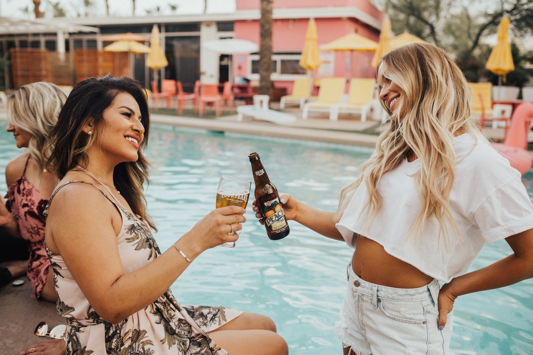 woman on pool tosing liquor with woman at daytime