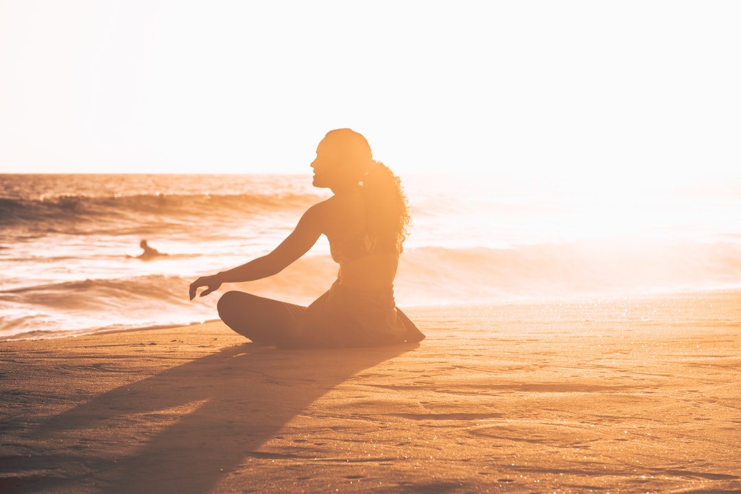 silhouette of woman sitting by the seashore during sunset