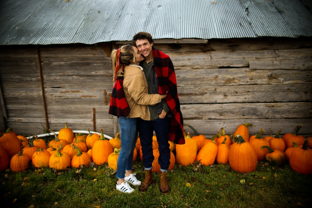 woman kissing man near pumpkins