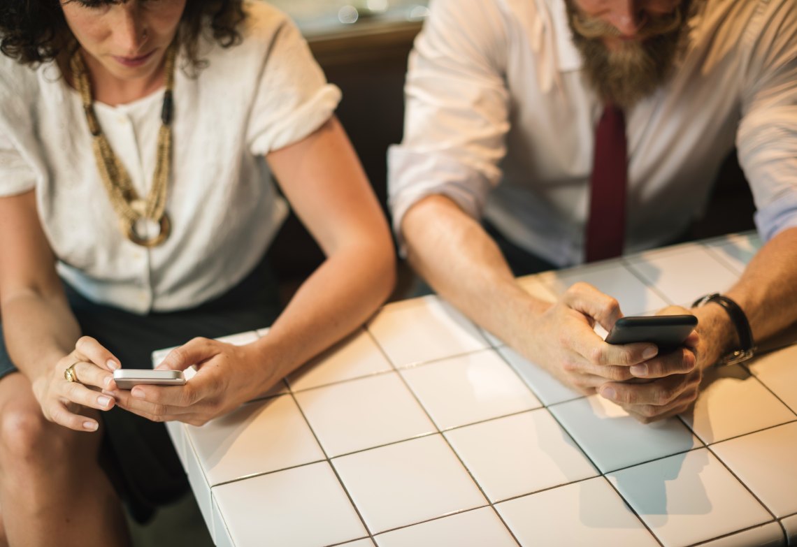 A man and a woman sitting side-by-side on their phones