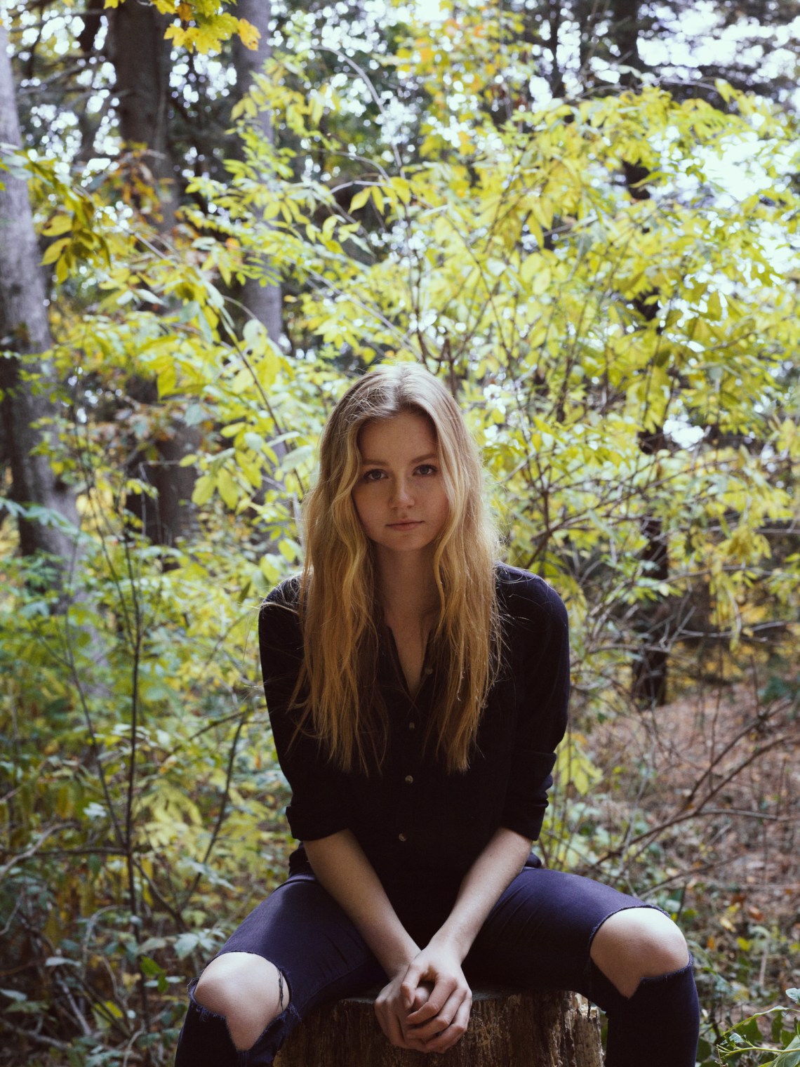 Girl sitting on a tree stump, holes in her jeans