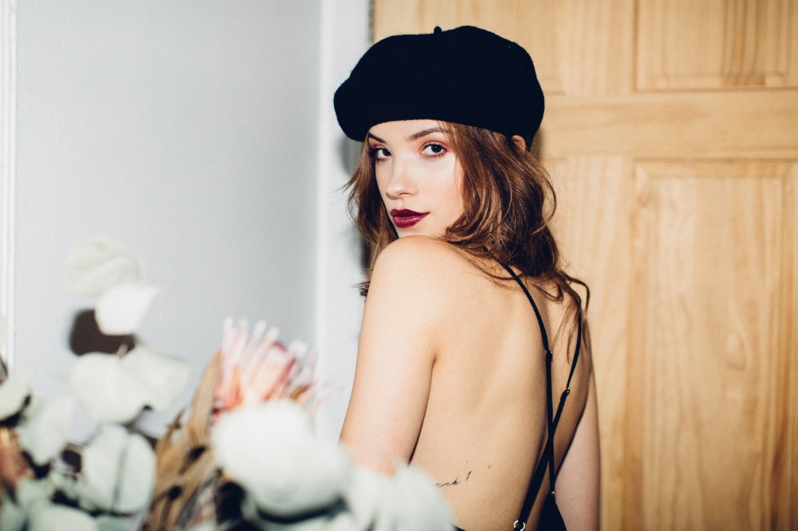 Girl in black hat, dark red lipstick, looking seductively or knowingly back at the camera