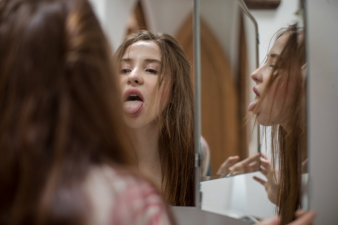 Girl inspects her tongue, sticking it out in the mirror