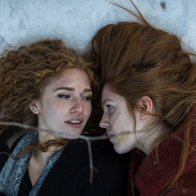 two women lock eyes as they lay together on the snowy ground