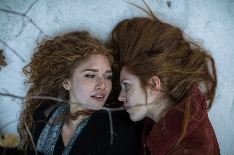 two women lock eyes as they lay together on the snowy ground