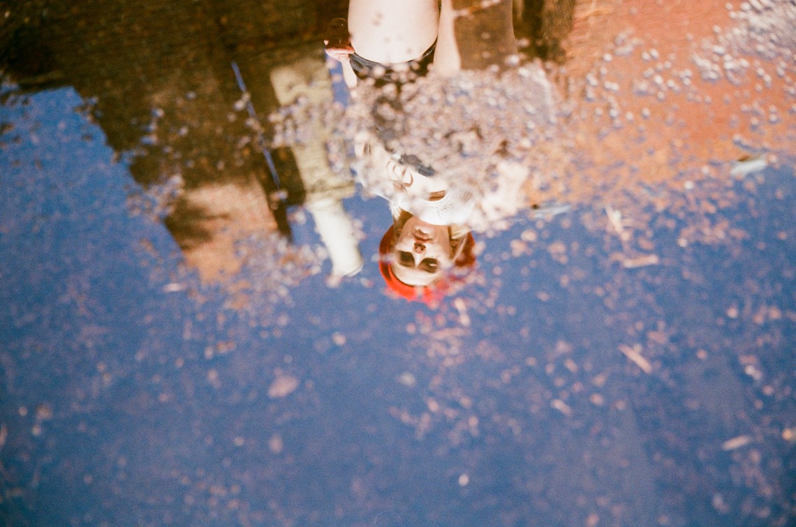 woman standing looking at self in puddle