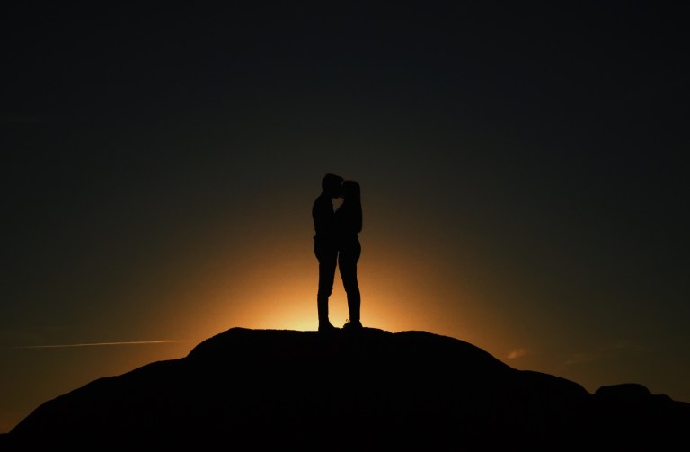 Man and woman stand in the dark on the horizon holding each other close