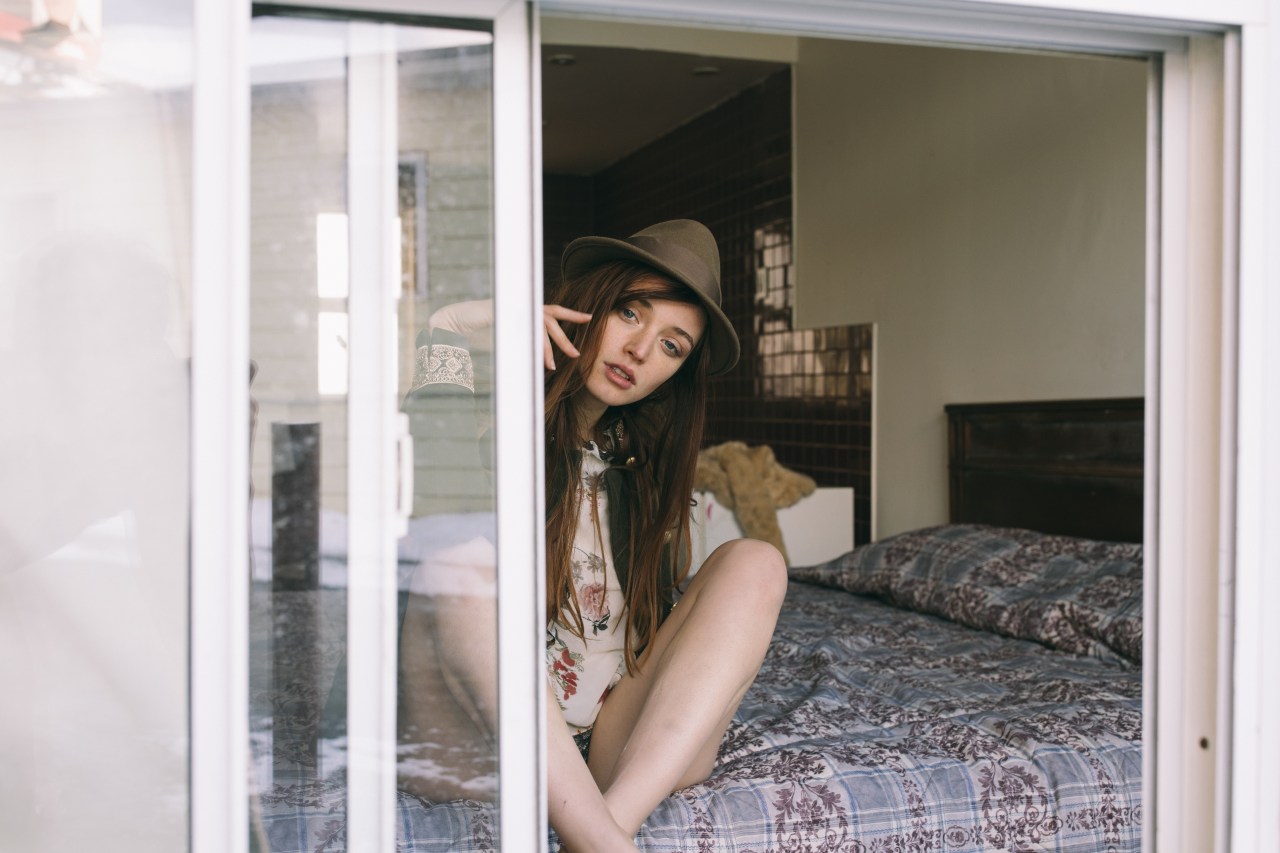 woman peering out window while sitting on bed