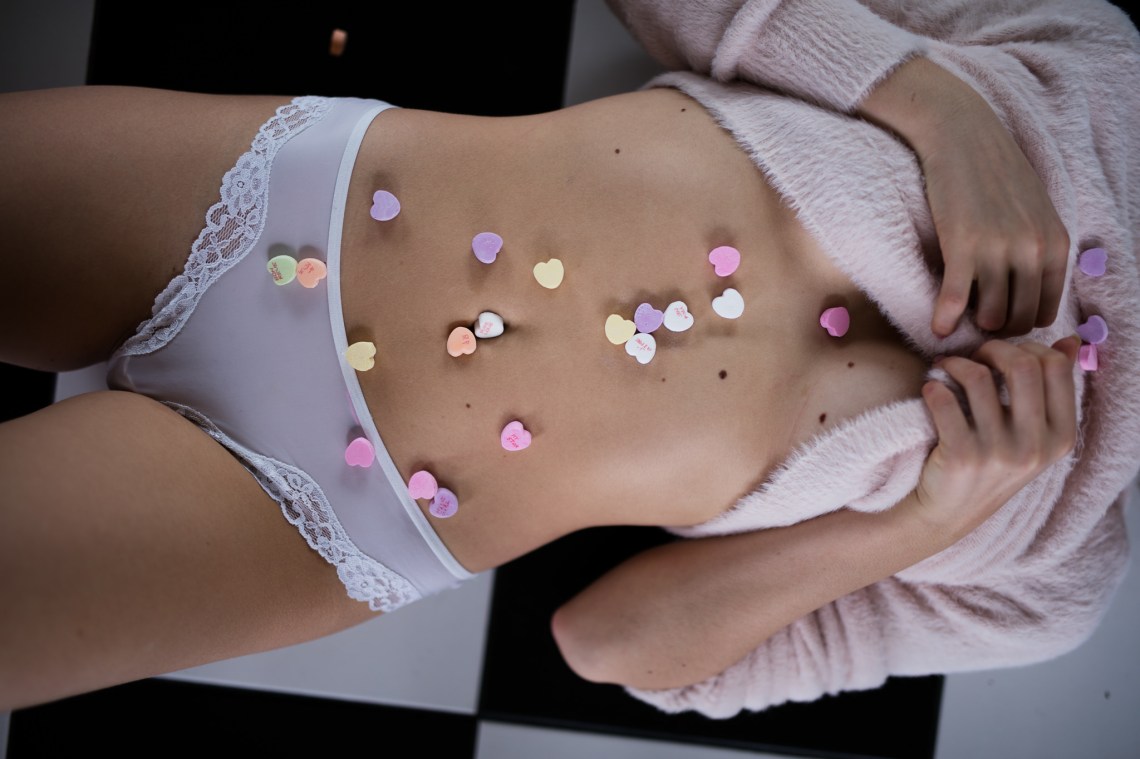 A woman in her underwear lays down with candy Valentine's hearts on her body