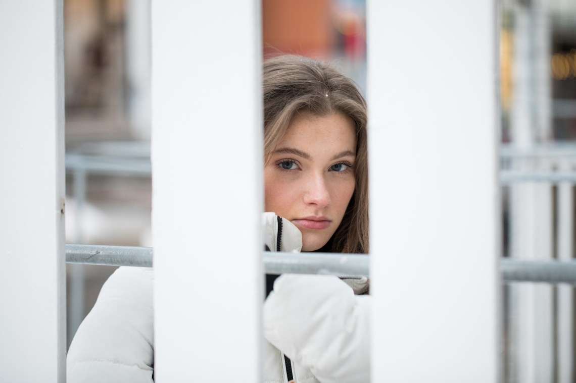 girl in white coat looking through fence