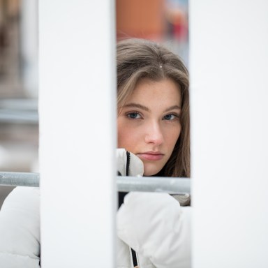 girl in white coat looking through fence