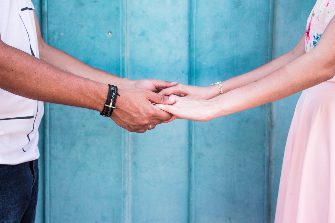 A man and a woman hold hands in front of a blue background