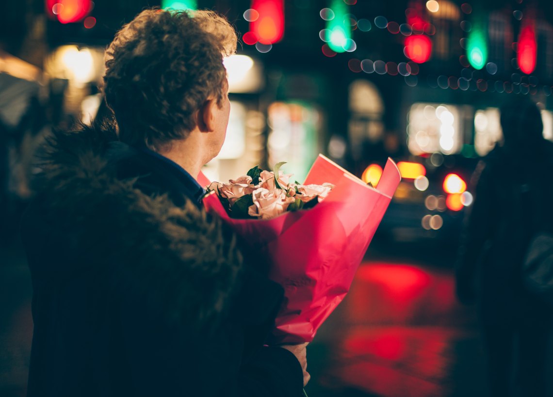 A man holds flowers in the night with lights blurring around him