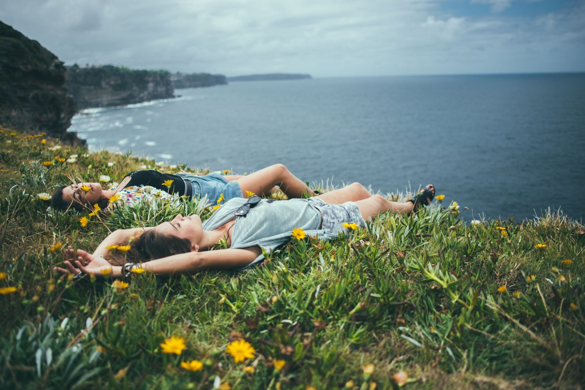 Two girls laying in the yellow flower speckled grass on an ocean bluff