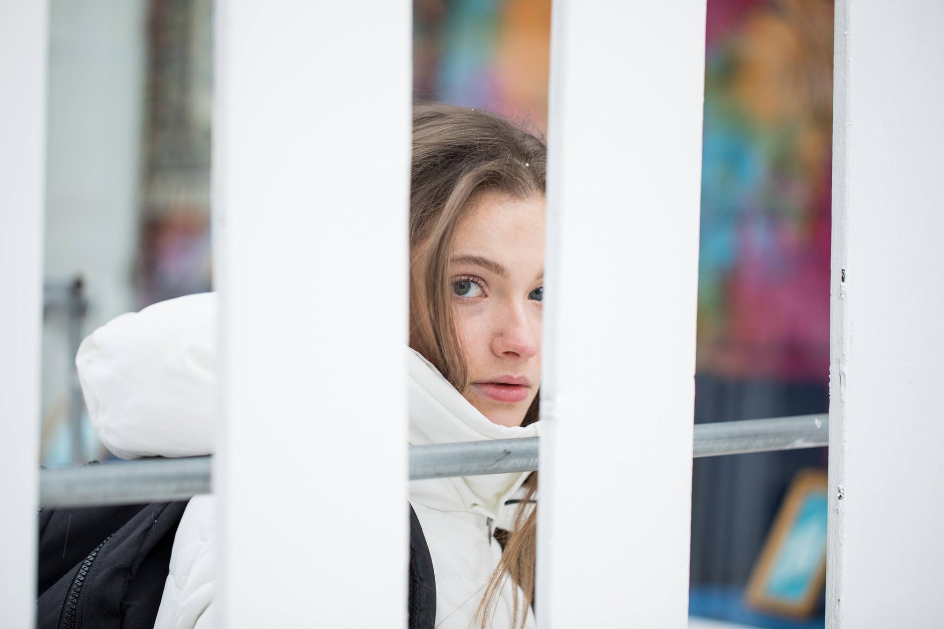 Girl in a white coat looking back from behind the fence