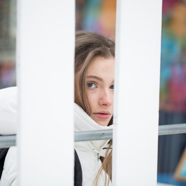 Girl in a white coat looking back from behind the fence