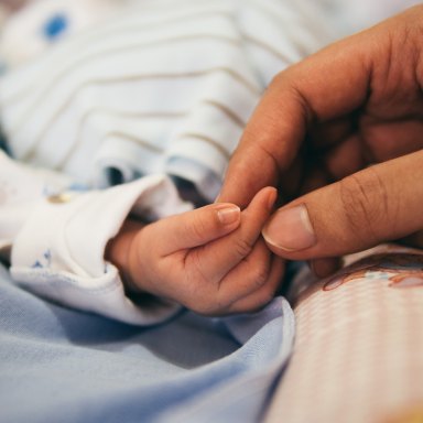 A baby and his parent hold hands