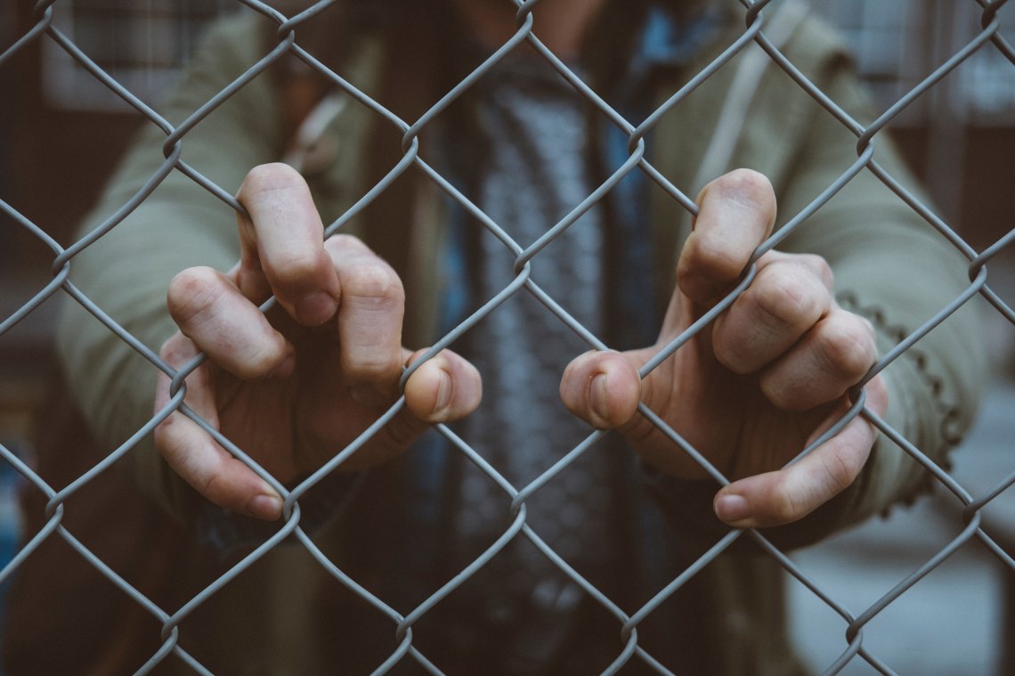 A person stands behind a chainlink fence, holding on with their hands